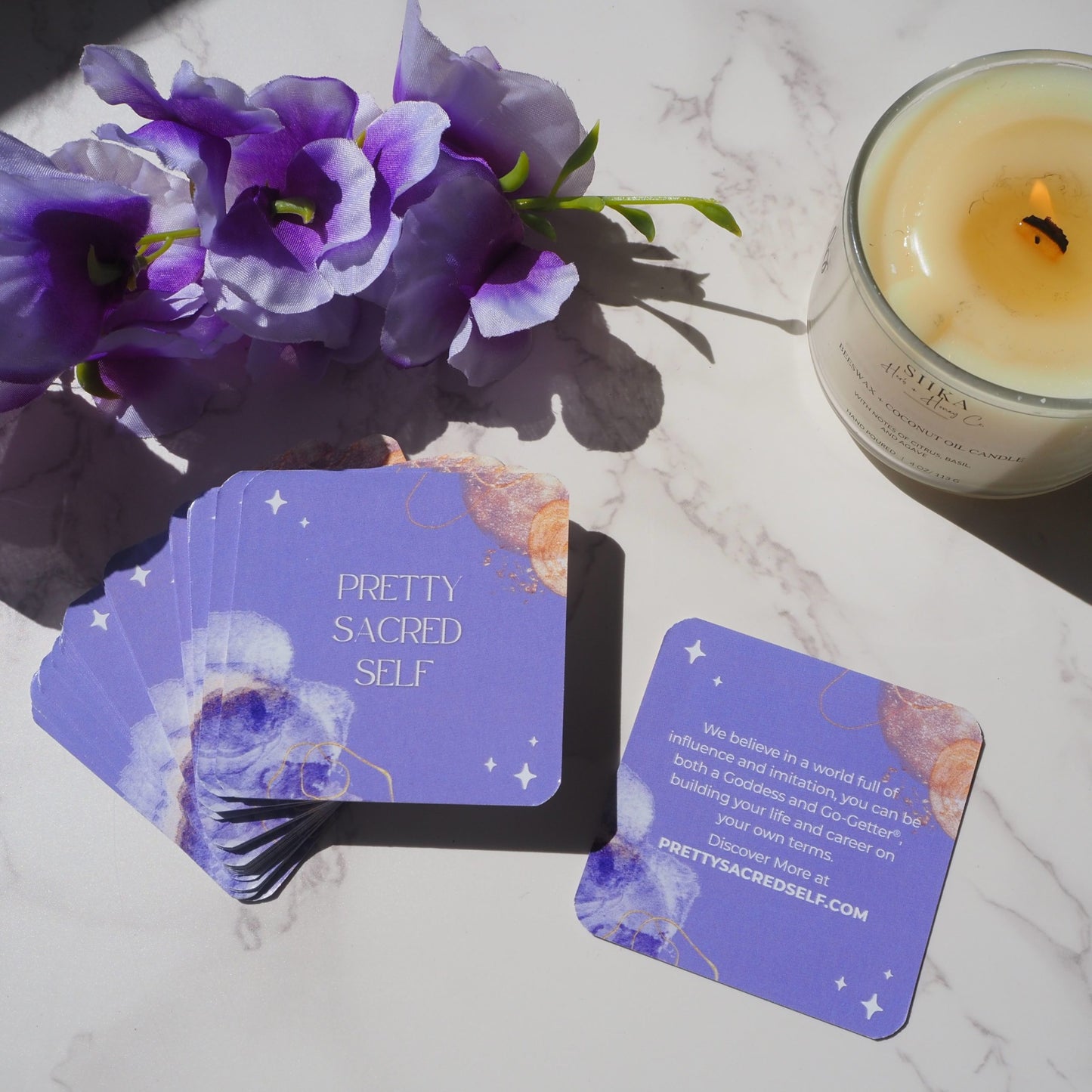 Purple cards with 'Pretty Sacred Self' branding on a marble surface with flowers and a candle.